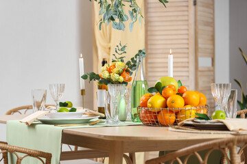 Table setting with citrus fruits, bottles of drink and flowers in living room. Closeup