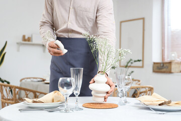 Male waiter putting vases with flowers on table in restaurant