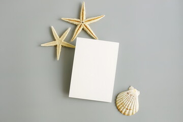 Empty paper blank card mockup, seashell, stars frame top view on grey background. Summer vacation,...