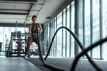 Woman performs battle rope workout in modern gym during afternoon sessions