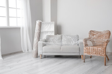 Wrapped furniture with stretch film in light room on moving day