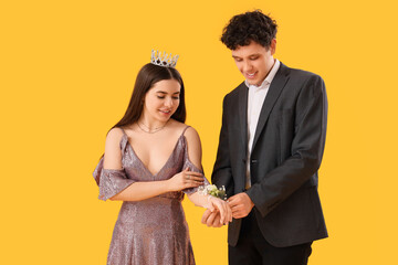 Young boy tying corsage around his prom date's wrist on yellow background