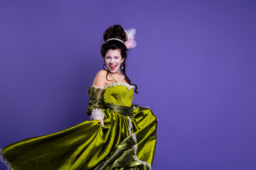 Obraz premium Elegant young woman in a green historical dress, posing with a playful expression on a violet background