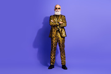 Charismatic Elderly Man in Extravagant Golden Suit on Purple Studio Background Standing Confidently with Folded Arms