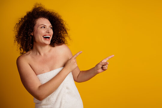 Confident young woman in a towel pointing with joy on yellow background celebrating self acceptance and beauty of natural femininity