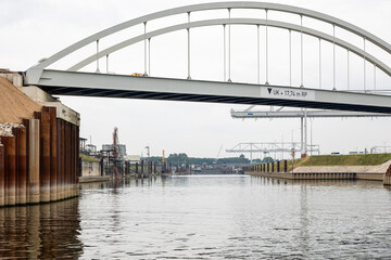 Waterway beneath a modern bridge with industrial structures along the banks