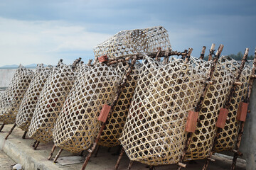 Coastal Fishing Baskets: Woven fishing baskets, lined up on a pier under a cloudy sky, represent a moment of coastal life. These tools stand ready for the next fishing trip. 