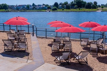 Sunny beach area with red umbrellas and lounge chairs by the river Rhine in summer