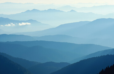Fototapeta premium Misty mountain panorama with soft light and layered blue peaks.
