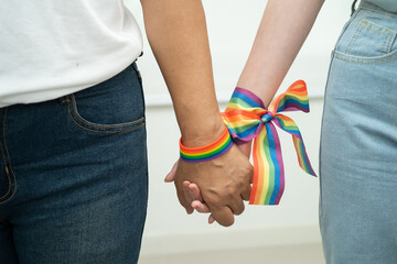 Asian LGBT couple woman holding hand wearing rainbow wristband.