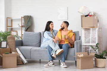 Happy young couple with coffee cup resting in room on moving day