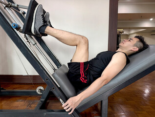Asian guy doing leg exercise, by using a leg press machine. To train thigh, glutes, quadriceps muscle. Gym workout and fitness photography pose. Muscle building for a healthy lifestyle. Leg day