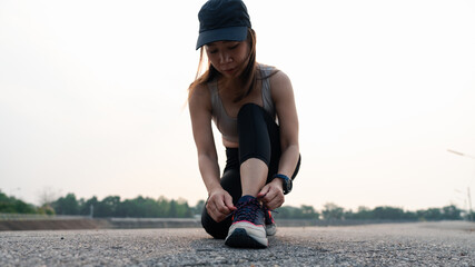 A woman ties her shoelaces while preparing to run on an empty road, showcasing determination and...