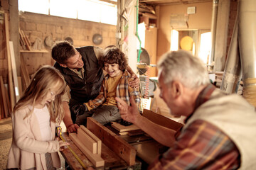 Grandfather teaching woodworking to grandkids with father in family workshop