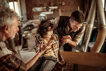 Happy grandfather teaching grandson carpentry with father in workshop