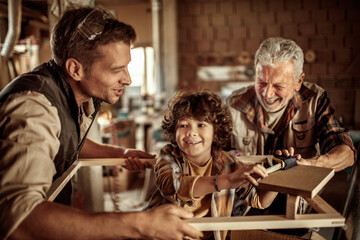 Happy grandfather teaching grandson carpentry with father in workshop