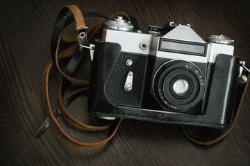 The Classic Vintage Old shabby Photo Camera in a black case open lens brown natural leather Strap on  Wooden table