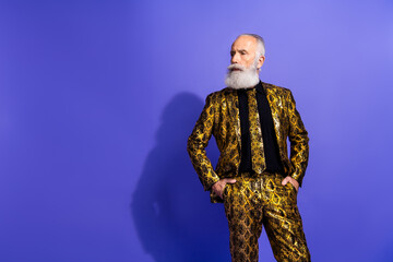 Stylish elderly gentleman in gold suit posing confidently against a solid purple backdrop expressing charisma and elegance