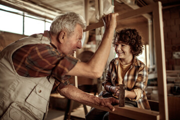 Grandfather carpenter teaching his grandson how to work with wood in a wood workshop