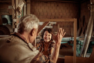 Grandfather carpenter teaching his grandson how to work with wood in a wood workshop