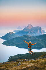 Man jumping enjoying mountains view travel solo in Norway active adventure vacations, tourist backpacker hiking healthy lifestyle freedom awakening concept dreamy sunset islands and sea landscape