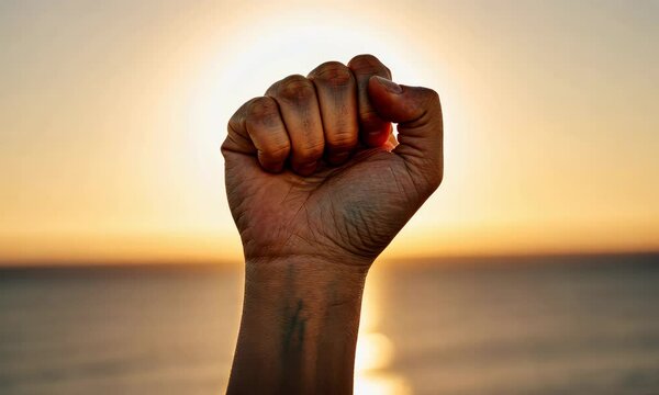 Close-up of raised clenched fist against sunrise, symbolizing strength and unity