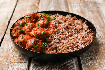 Tasty meatballs with sauce and brown rice on wooden table, closeup