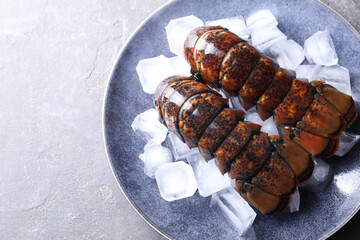 Raw lobster tails with ice on grey table, top view. Space for text