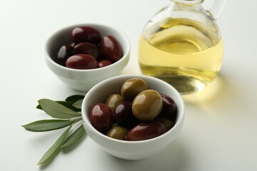 Tasty marinated olives, leaves and oil on white table, closeup