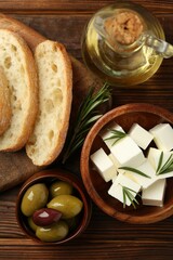 Delicious marinated olives, bread and feta cheese served on wooden table, flat lay