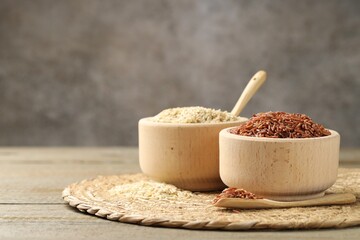 Different sorts of raw brown rice on wooden table against grey background, closeup. Space for text