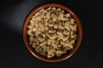close up image of a bowl of raw cashew nuts over a dark background, view from above