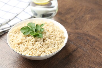 Delicious brown rice with parsley served on wooden table, closeup. Space for text
