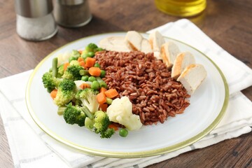 Delicious brown rice with chicken and vegetables served on wooden table, closeup