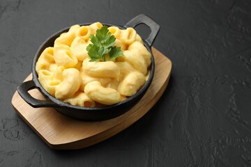 Delicious macaroni and cheese with parsley on black table, closeup