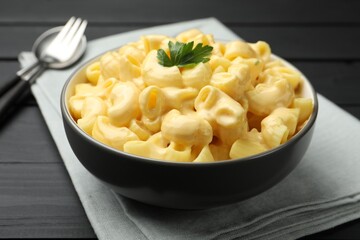 Delicious macaroni and cheese with parsley served on black wooden table, closeup
