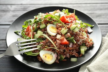 Delicious salad with brown rice on black wooden table, closeup