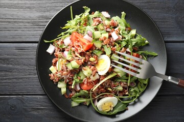 Delicious salad with brown rice on black wooden table, top view