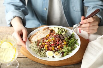 Woman eating delicious salad with brown rice at wooden table, closeup