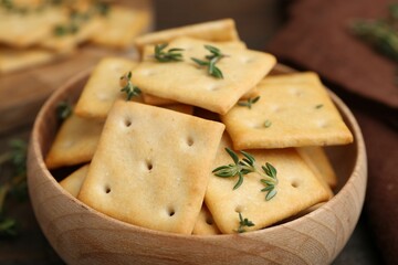 Tasty salty crackers with thyme on wooden table, closeup