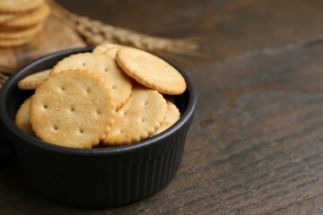 Tasty salty crackers and wheat spikes on wooden table, closeup. Space for text