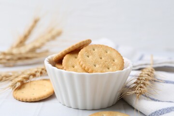 Tasty salty crackers with wheat spikes on white tiled table, closeup