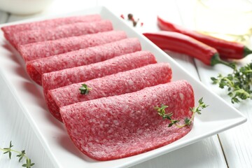 Slices of tasty smoked sausage and spices on white wooden table, closeup