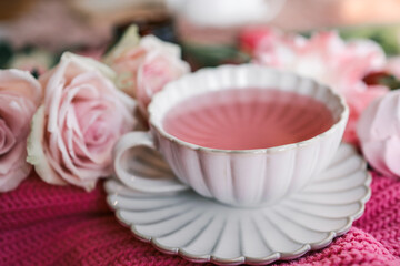 Elegant ceramic cup with pink tea on a matching saucer, surrounded by fresh tulips, roses, and cozy textures. Feminine flat lay with soft pastel tones and romantic spring vibes