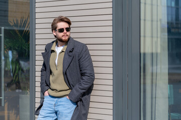 Fototapeta premium Stylish man in fashionable outerwear stands outside a modern building