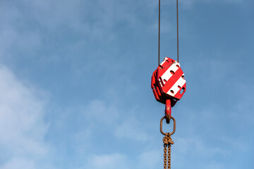 Heavy crane block hook hangs in the bright sky over construction site