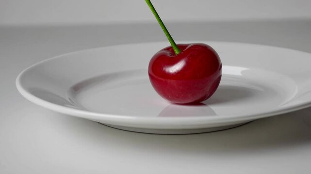 Minimalist video concept featuring a single cherry on a white plate. Captured from a side angle, emphasizing simplicity and elegance.Live desktop wallpaper.