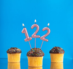 Three birthday cupcakes with number 122 candle - Blue background