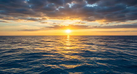 Obraz premium Ocean sunset: golden sun dips below the horizon, casting a shimmering reflection on the blue waves under a dramatic, cloudy sky. 