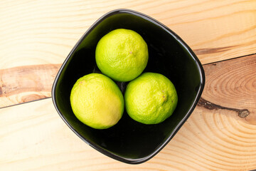 Sour juicy limes with a ceramic plate on a wooden table, close-up, top view.